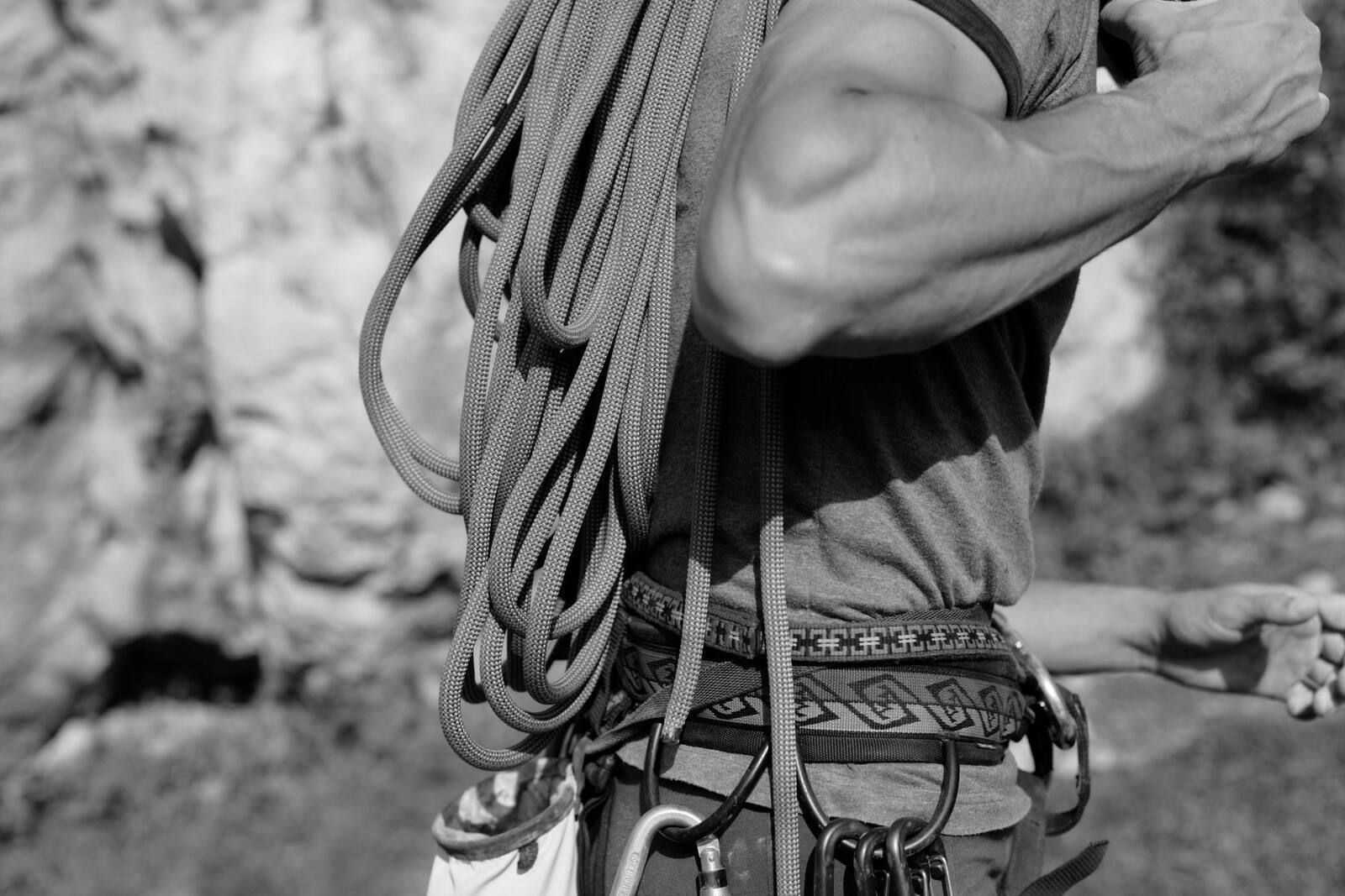 A climber with a coiled rope over one shoulder, harness, chalk bag and carabiners
